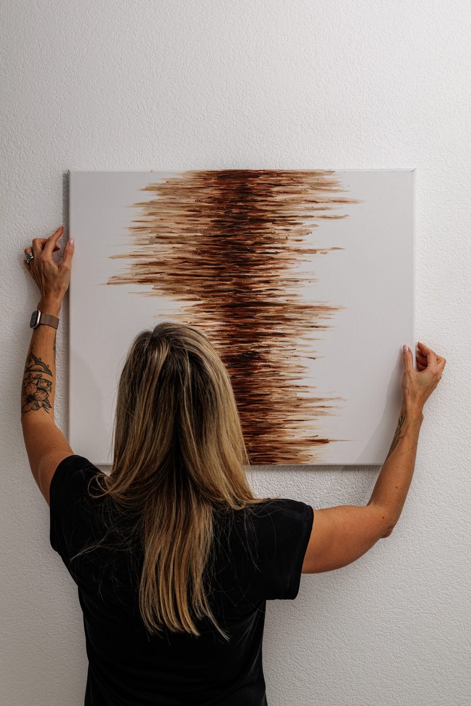 Francine Berthod accroche une toile sur un mur blanc, les deux mains sur le châssis.